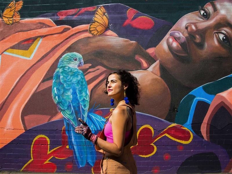 A picture of street artists Katherine Gailer standing in front of one of her murals, of a woman