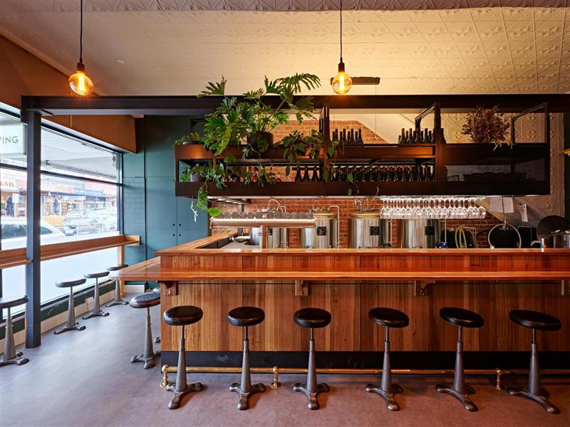 A bar with a row of seats in front, and several bottles and glasses in the background